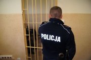 policjant zamyka kratę pomieszczenia dla osób zatrzymanych