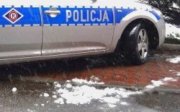 bok policyjnego radiowozu z napisem policja i logiem ruchu drogowego. Na nawierzchni widoczny śnieg.