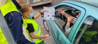 policjantka i pierwszoklasista wręczają kierowcy ulotkę z informacjami o zmianach w przepisach ruchu drogowego