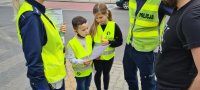 chłopiec i dziewczynka w towarzystwie policjantów wręczają pieszemu ulotkę informacyjną o zmianach w przepisach ruchu drogowego