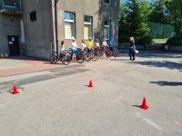 na zdjęciu widoczny fragment toru przeszkód dla uczniów przystępujących do egzaminu na kartę rowerową. W tle policjantka rozmawiająca z dziećmi na rowerach.