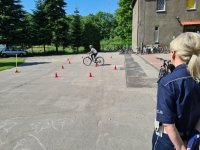 policjantka przygląda się jak dziewczynka na rowerze pokonuje tor przeszkód podczas egzaminu na kartę rowerową