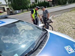 policjant ruchu drogowego w rozmowie z rowerzystą, który w przednim koszyku przewoził psa