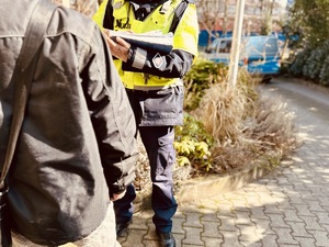 zdjęcie przedstawia zatrzymanego mężczyznę, któremu policjanci wypisują mandat. W tle widoczny radiowóz