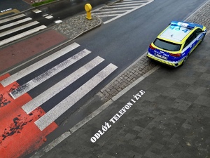 zdjęcie przedstawia radiowóz stojący przy przejściu dla pieszych, przed przejściem na chodniku napis Odłóż telefon i żyj.